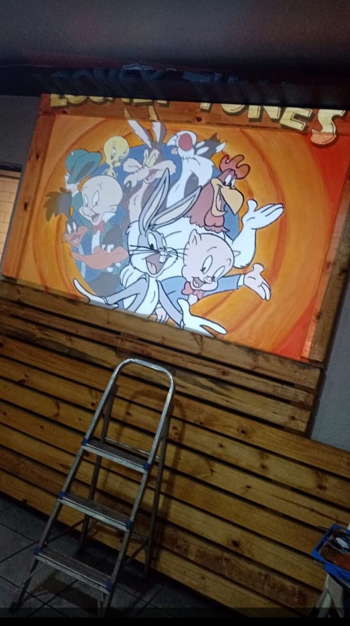 Hand-painted cartoon character mural in progress on the kids area wall at Amigos, with a step ladder in front
