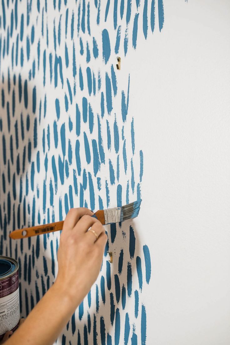 Close-up of an artist hand-painting individual blue brushstrokes onto a white wall with a flat brush