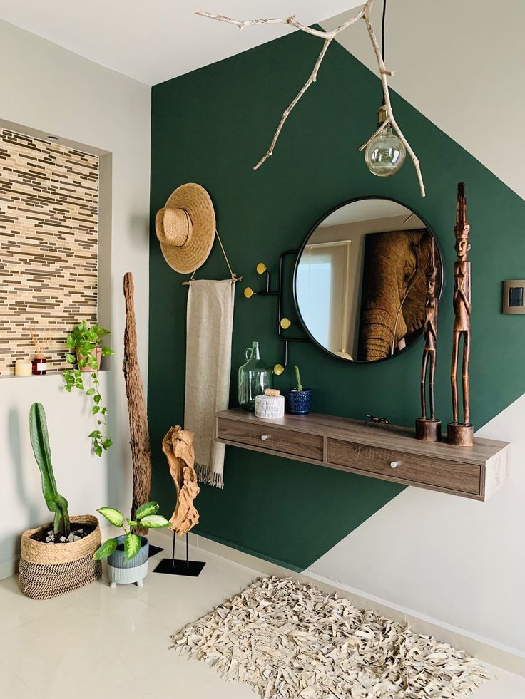 Deep green angular painted feature wall in an entrance hallway, framing a round mirror, floating timber shelf and natural decor
