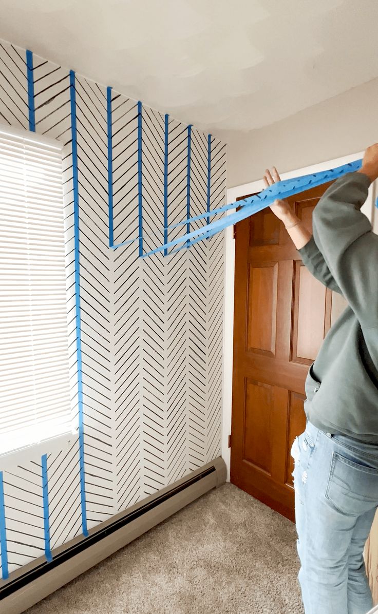 Artist masking out a blue herringbone pattern with painters tape across a bedroom wall before painting