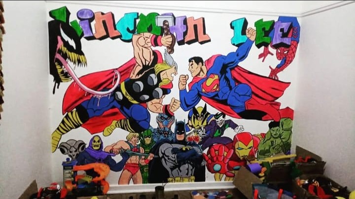 Hand-painted comic book superhero mural wrapping two bedroom walls, with children's names in colourful graffiti lettering above