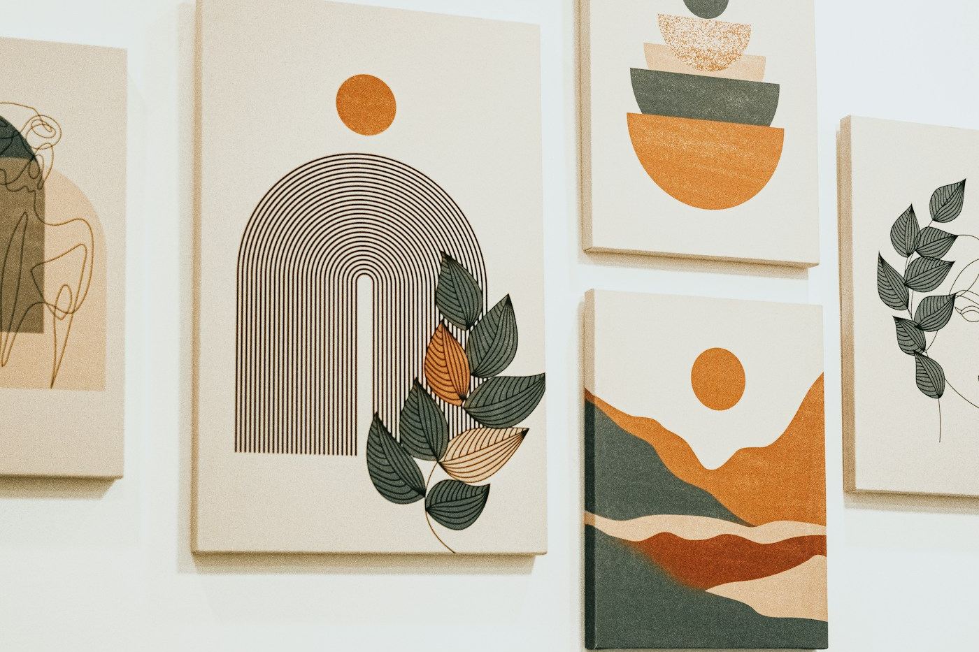 A group of bespoke decorative art panels in muted terracotta, sage and cream arranged across a white wall